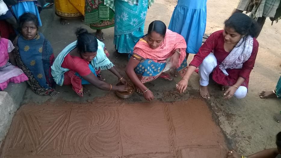 Sanghamitra squatting with two other women on the dirt writing on mud