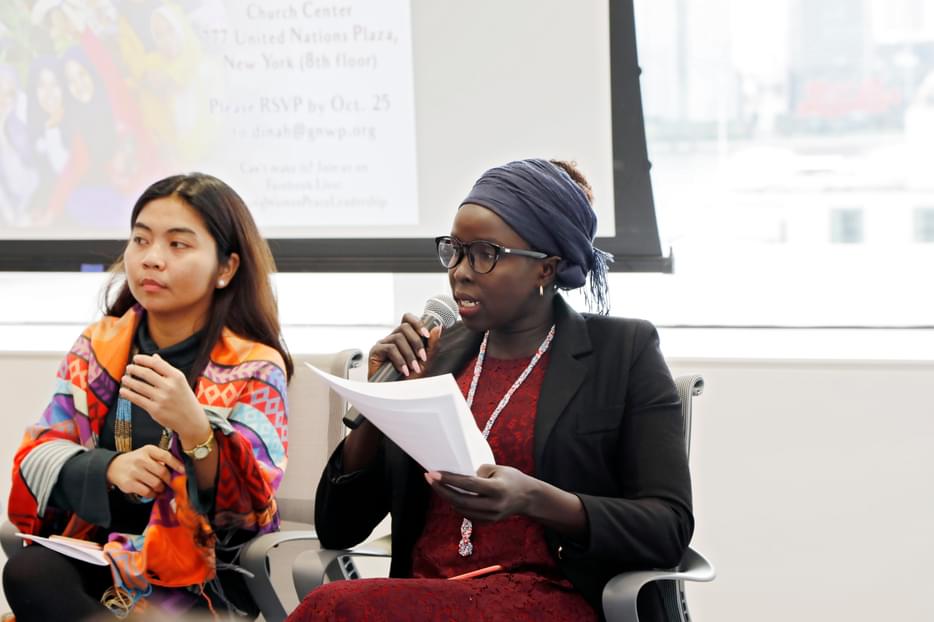Suzy speaking with a mic in her hand sitting on a panel at an event