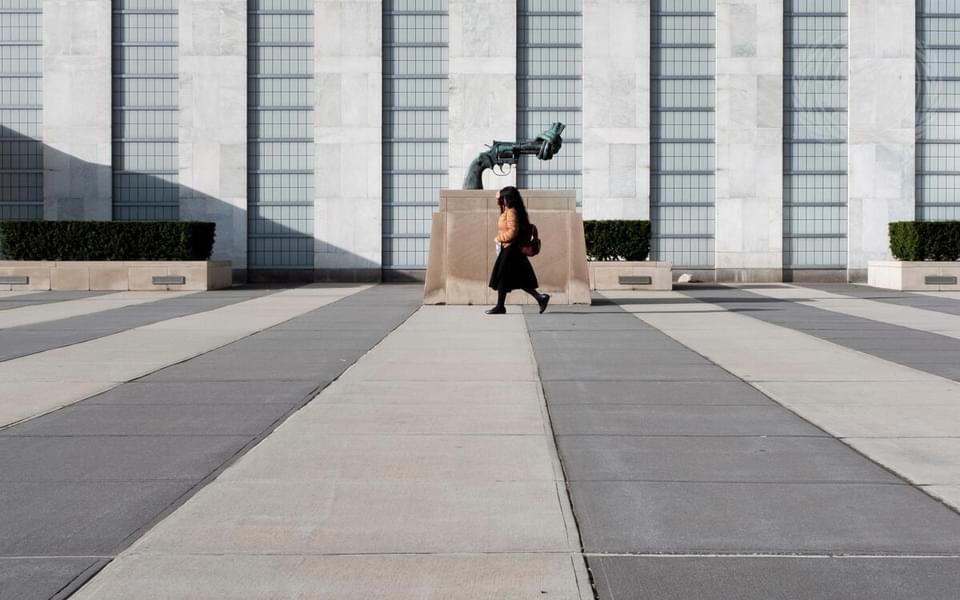A woman walking in front of a statue of a gun with a knot tied at the end at the United Nations headquarters