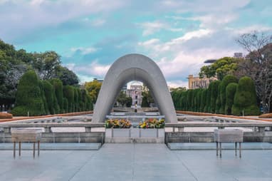 Hiroshima peace memorial seen under an arch statue with a burning flame and flowers in front
