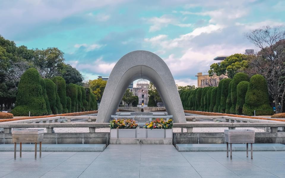Hiroshima peace memorial seen under an arch statue with a burning flame and flowers in front