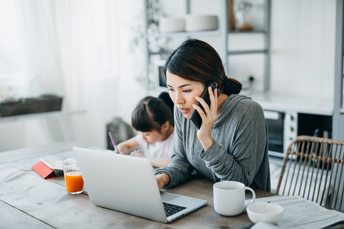Woman on the phone while at her computer while child plays in the background