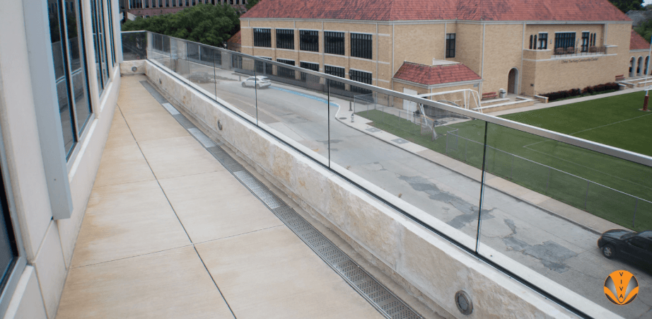 Glass railing along a modern building balcony with a campus view.