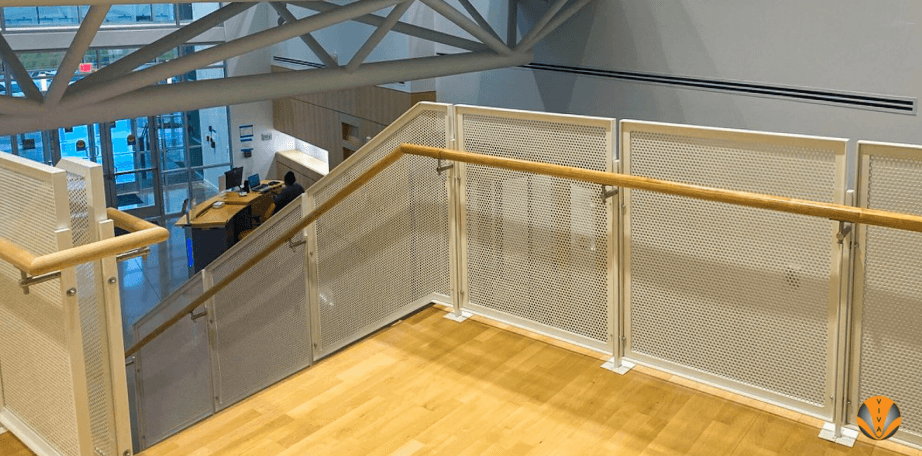 Upper-level railing with wood handrails and perforated metal panels in a bright, open atrium.