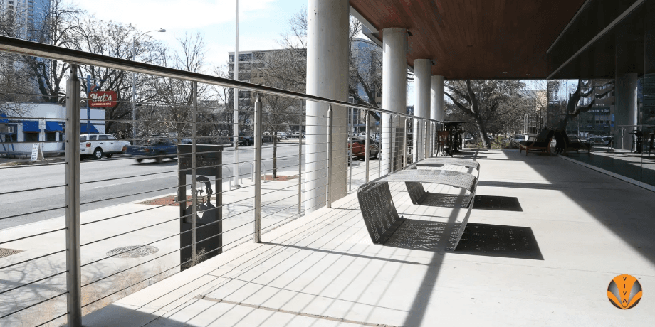 Stainless steel cable railing along a city sidewalk with modern benches.