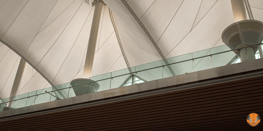 Sleek glass balcony railing with no visible frame under a large architectural canopy.