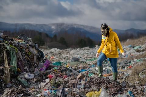 Woman with gas mask walking on landfill environme R