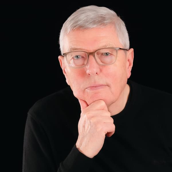 Author Alan Johnson in a black jumper looking into the camera. He is Caucasian, with blue eyes, grey hair, grey glasses and is leaning on his hand. He is pictured against a black background.