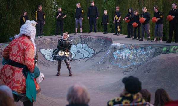 Lloyd Notice as Alonso and Elizabeth Crarer as Antonia, standing in a skate park. The young company are standing behind, some holding basketballs